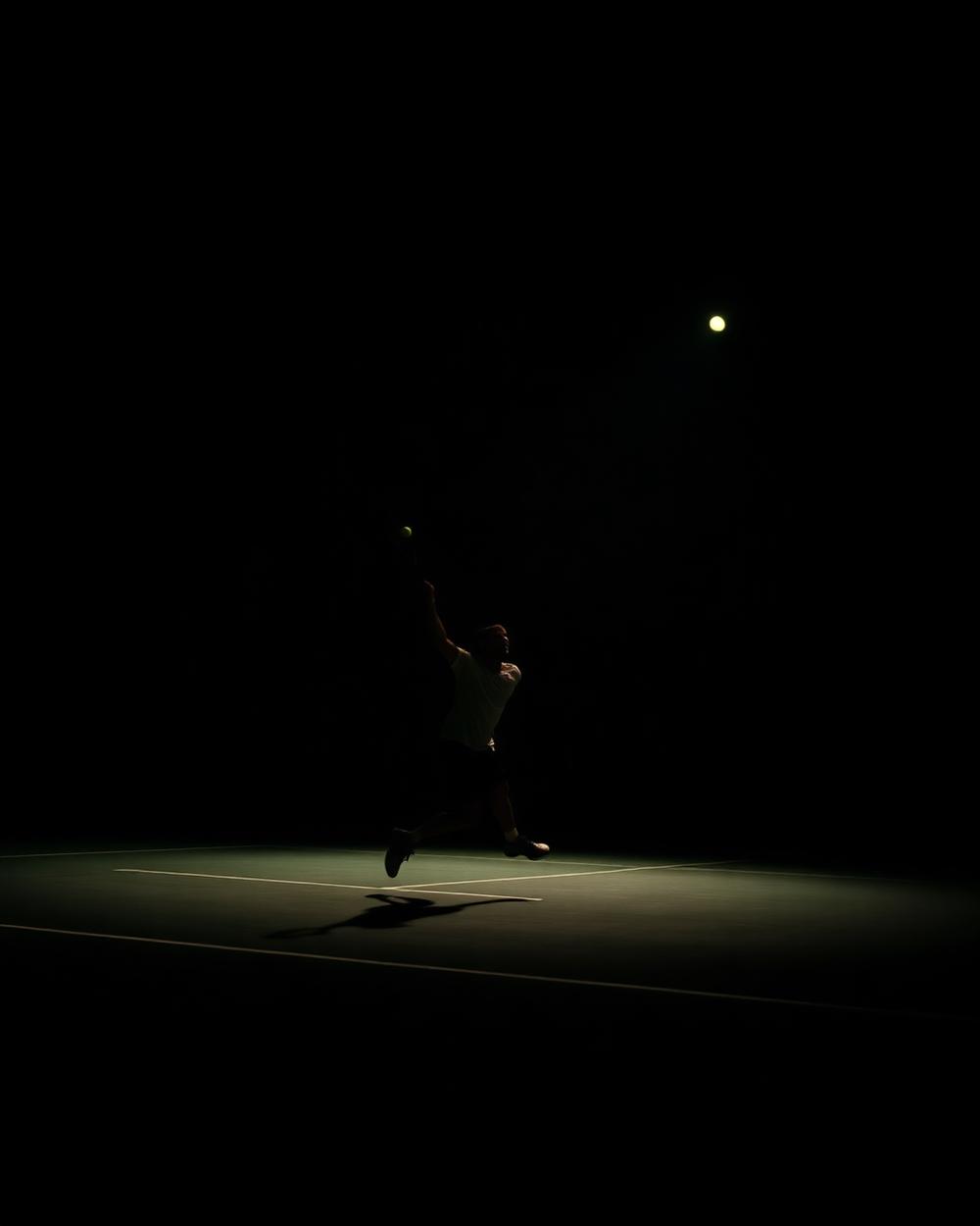 A racket-sport athlete serving on a floodlit court at night